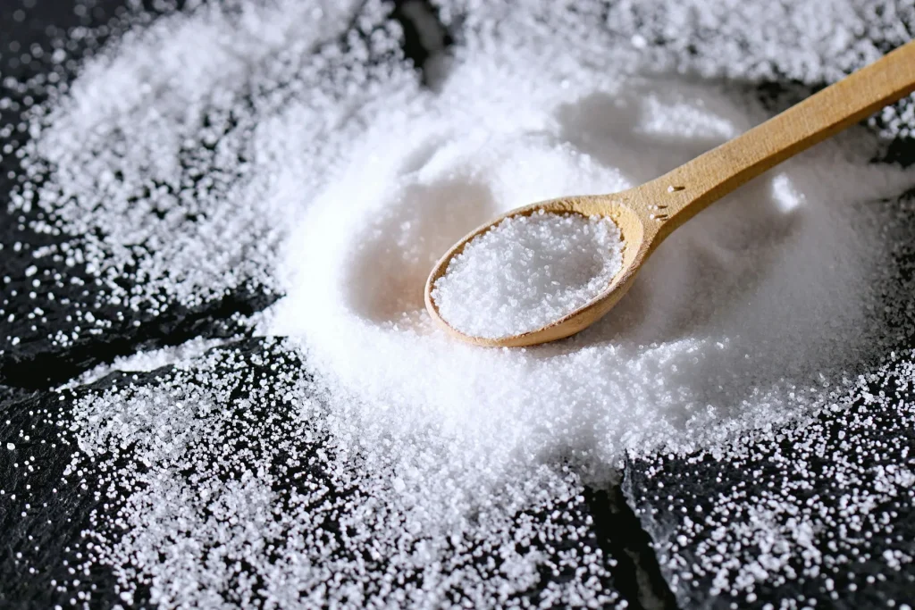 Close-up of white iodised salt in a wooden spoon on a dark surface.
